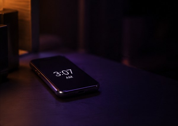 A phone glowing on a nightstand at 3:07 a.m.