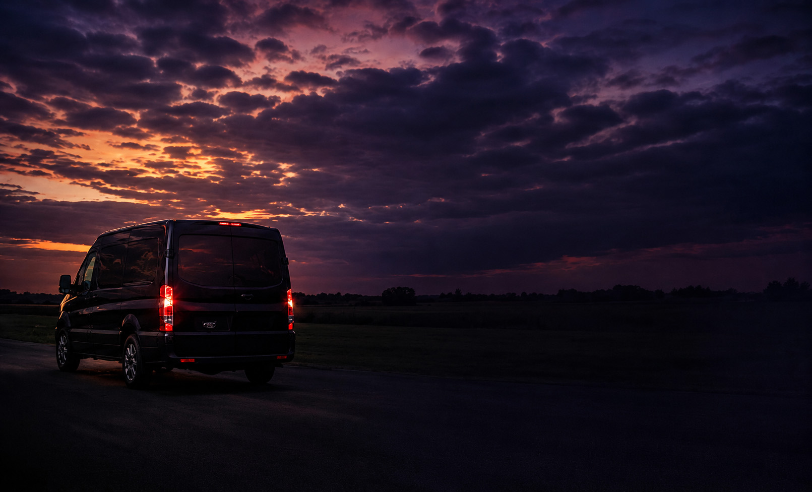 A transport van on an open road beneath a purple sunset sky